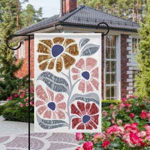 Può includere: Una bandiera da giardino bianca con un motivo floreale. I fiori sono in tonalità di marrone, rosa e rosso con centri blu. Le parole "FUCK TRUMP" sono incorporate nei petali e nelle foglie dei fiori.