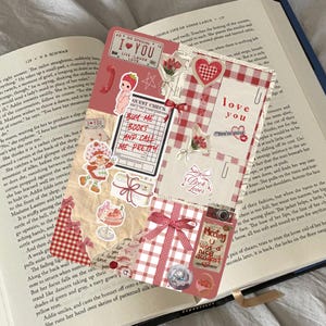 Könnte beinhalten: Eine Collage aus Aufklebern und Papierelementen auf einem offenen Buch. Das Design umfasst ein Erdbeermotiv, rotes Vichy-Karo und den Text "Buy Me Books and Call Me Pretty."