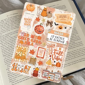 Può includere: Un foglio di adesivi a tema autunnale con zucche, foglie e le frasi "Books Over Boos", "In My Cozy Girl Era", "Fall Vibes" e "Spooky Season". Gli adesivi sono nei toni dell'arancione, marrone e bianco.