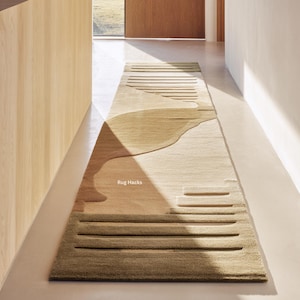 Può includere: Un lungo tappeto rettangolare dal design moderno. Il tappeto presenta una palette di colori beige, marrone chiaro e verde oliva. Il design include linee orizzontali e forme astratte. Il tappeto è posto in un corridoio.