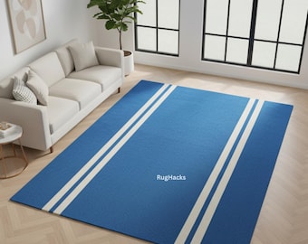 May include: A rectangular blue rug with two wide, parallel white stripes running lengthwise. The rug is placed on a light-colored hardwood floor. The text "RugHacks" is visible on the rug.