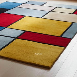 May include: A rectangular area rug with a geometric design. The rug features a pattern of colorful rectangles in shades of yellow, red, blue, and gray, outlined with black borders. The rug is made of a soft, textured material.