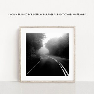 May include: Black and white photograph of a winding road through a forest shrouded in fog. The road has white lane markings and is framed by trees on both sides. The text at the top reads: SHOWN FRAMED FOR DISPLAY PURPOSES - PRINT COMES UNFRAMED.