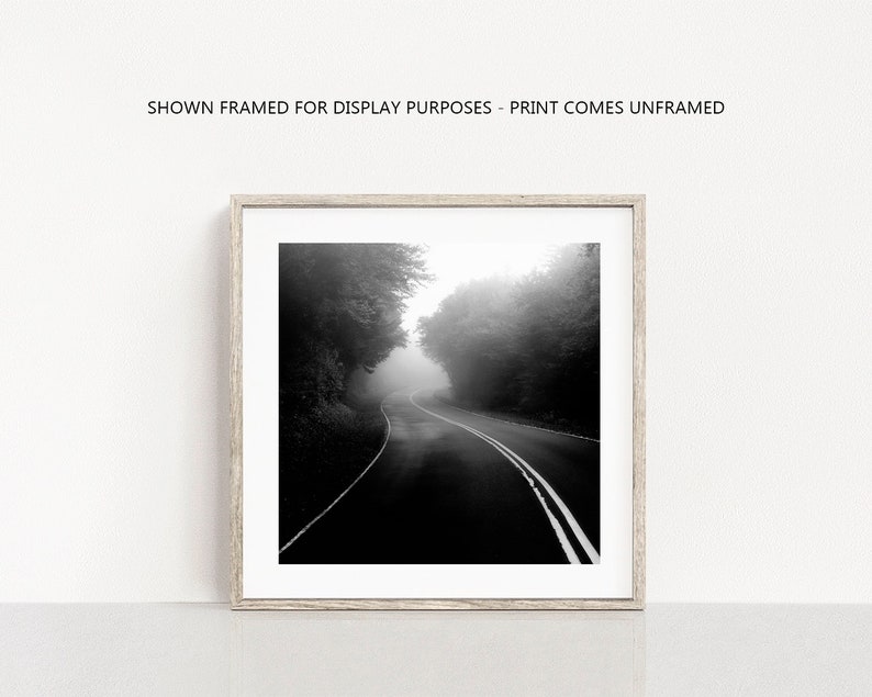 May include: Black and white photograph of a winding road through a forest shrouded in fog. The road has white lane markings and is framed by trees on both sides. The text at the top reads: SHOWN FRAMED FOR DISPLAY PURPOSES - PRINT COMES UNFRAMED.