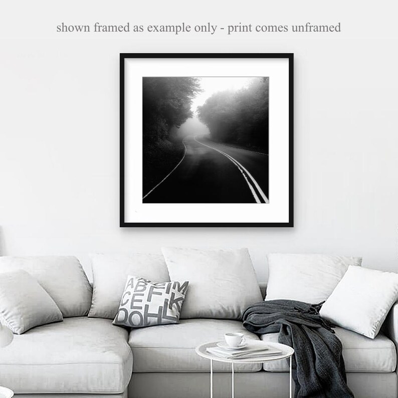 May include: Black and white framed print of a road disappearing into a foggy forest. The road has white lines and is surrounded by trees. The text at the top says "shown framed as example only - print comes unframed."