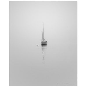 Op de afbeelding: Een zeilboot ligt voor anker in een stil water op een mistige dag. Een enkele eend zwemt in de verte.