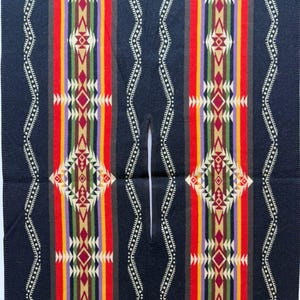 May include: A dark navy blue poncho featuring a central vertical slit opening. The garment is decorated with symmetrical, colourful geometric patterns in red, yellow, green, purple, and cream, arranged in repeating vertical stripes and diamond shapes.