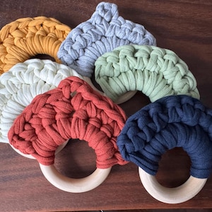May include: A set of six crocheted teething rings in various colors, including yellow, gray, green, red, white, and blue. Each ring has a wooden handle.