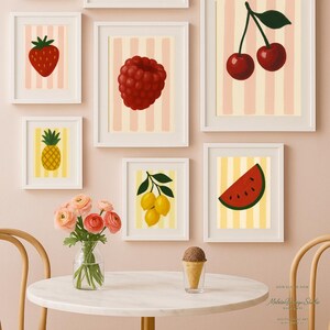Könnte beinhalten: Eine Sammlung gerahmter Kunstdrucke mit Früchten, darunter eine Erdbeere, eine Himbeere, Kirschen, eine Ananas, Zitronen und eine Wassermelonen-Scheibe. Jeder Druck zeigt eine Fruchtillustration vor einem gestreiften Hintergrund, in einem weißen Rahmen.