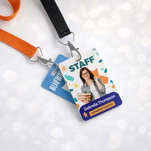 May include: Two rectangular plastic ID badges attached to lanyards. One badge is blue with white text, while the other is white with colorful abstract shapes, the word STAFF, a photo of a person holding books, and the text Gabreila Thompson ADMINISTRATOR.