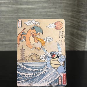 以下が含まれることがあります： 日本の浮世絵風イラストの、CharizardとBlastoiseが描かれたトレーディングカード。Charizardはオレンジ色、Blastoiseは青色で、背景には山と海が描かれています。カードには日本語のテキストも表示されています。