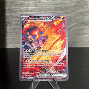 May include: A Pokémon trading card featuring Moltres ex with a fiery design. The card displays the text "Flame Screen" and "Evil Incineration" with a HP of 220. The card is displayed on a clear plastic stand.