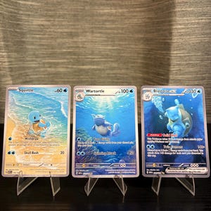 May include: Three Pokémon trading cards featuring Squirtle, Wartortle, and Blastoise. The Squirtle card shows the character on a beach, the Wartortle card shows it underwater, and the Blastoise card has it in a dark blue underwater scene.