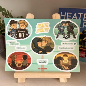 Könnte beinhalten: Ein türkisfarbener Druck mit Cartoon-Illustrationen von zwei männlichen Figuren in verschiedenen Szenen. Der Druck enthält Textblasen mit Sätzen wie "Heated Rivalry" und "Sleepy Nima".