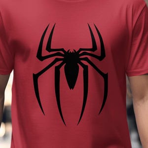 Puede incluir: Una camiseta roja con un gran dise&ntilde;o de ara&ntilde;a negra. La ara&ntilde;a es una silueta con ocho patas y un cuerpo central. La camiseta es de manga corta y parece estar hecha de un material suave. El dise&ntilde;o est&aacute; centrado.