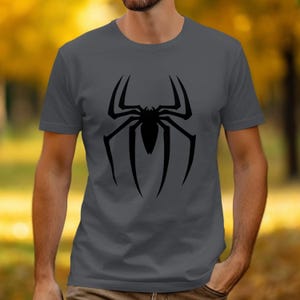 Puede incluir: Camiseta gris con un gran dise&ntilde;o de ara&ntilde;a negra en la parte delantera. El dise&ntilde;o de la ara&ntilde;a es una ilustraci&oacute;n sim&eacute;trica y estilizada con patas largas y curvas y un cuerpo central. La camiseta es de color s&oacute;lido y tiene cuello redondo.