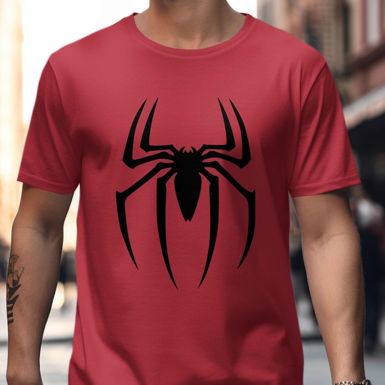 Puede incluir: Una camiseta roja con un gran dise&ntilde;o de ara&ntilde;a negra. La ara&ntilde;a es una silueta con ocho patas y un cuerpo central. La camiseta es de manga corta y parece estar hecha de un material suave. El dise&ntilde;o est&aacute; centrado.