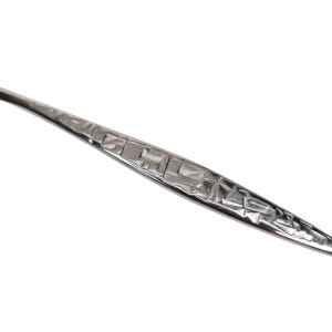 May include: Close-up of a silver utensil with a textured handle. The handle features a geometric pattern of squares and rectangles. The utensil has a polished, reflective surface, and is set against a white background.
