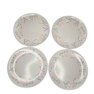 May include: Four round, off-white plates with a floral design. The plates feature a border of pink and blue flowers and leaves. The plates are arranged in a square formation, showcasing the decorative pattern.