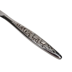 May include: Close-up of a stainless steel knife with a decorative geometric pattern on the handle. The knife has a polished finish and a sharp blade, suitable for cutting. The handle design adds a touch of elegance.