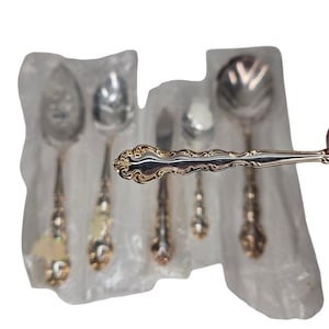 May include: Set of six silver and gold plated spoons with ornate handles. The spoons are wrapped in plastic and are ready for gifting.