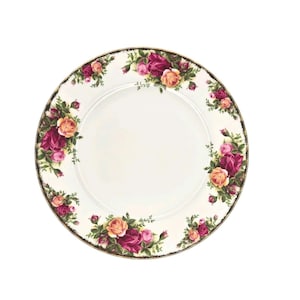 May include: A white ceramic plate with a floral rose design. The plate features a gold rim and a pattern of pink, red, and peach roses with green leaves. The roses are arranged around the edge of the plate.