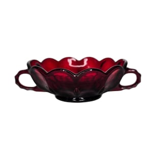 May include: A ruby red glass bowl with a scalloped rim and two handles. The bowl has a decorative, vintage design and is likely used for serving or display. The glass has a glossy finish.