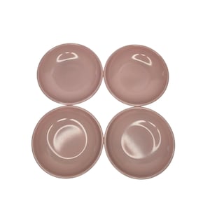 May include: Four matching, light pink ceramic bowls arranged in a square. Each bowl has a rounded shape with a slightly deeper center. The bowls are a solid, muted pink color, and the background is plain white.