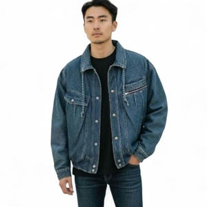 May include: A medium-wash denim jacket with a zip pocket and button closures. The jacket has a classic collar and a relaxed fit. The model is wearing a black t-shirt and dark wash jeans. The background is white.