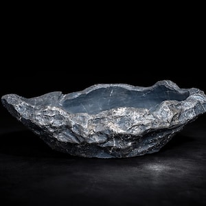 Könnte beinhalten: Eine dunkelgraue, steinartige Schale mit einer rauen, strukturierten Außenseite und einer glatten Innenseite. Die Schale hat eine unregelmäßige, organische Form und ist vor einem schwarzen Hintergrund platziert.