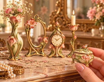 Könnte beinhalten: Eine Sammlung dekorativer Gegenstände mit Blumenmotiv in Rosa und Grün, bestehend aus einer Vase, einem ovalen Spiegel, einer Uhr, einem Kerzenhalter mit weißer Kerze und einer kleinen Schmuckdose mit Deckel im Vordergrund.