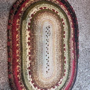 May include: Oval braided rug with a mix of colors including red, green, brown, and cream. The rug features a floral pattern and is approximately 48 inches long and 30 inches wide.
