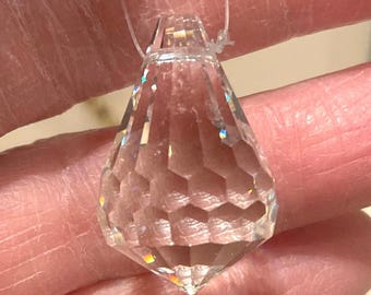 May include: Clear, faceted crystal pendant with a diamond-like shape, suspended by a thin, transparent cord. The crystal reflects light, creating a rainbow effect. The pendant is a decorative item.