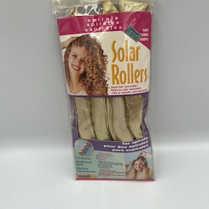 Puede incluir: Un paquete de herramientas de peinado Solar Rollers. El embalaje es rosa y morado con las palabras "Solar Rollers" en letras amarillas grandes. El paquete incluye varios rulos beige y una foto de una mujer con cabello rizado.
