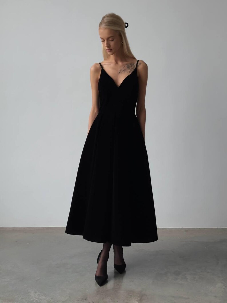 May include: A black midi dress with a V-neckline and spaghetti straps. The dress has a flared skirt and is paired with black heels. The image is set against a plain white background.
