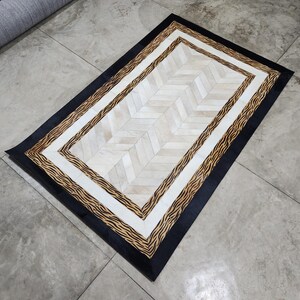 May include: Rectangular rug with a black border, zebra print accent, and a white and beige chevron pattern centre. The rug is made of natural materials and is suitable for a living room or bedroom.