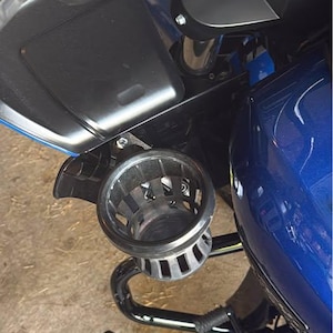 Puede incluir: Primer plano de una motocicleta con un dep&oacute;sito de combustible azul y accesorios negros. Un portavasos plateado est&aacute; montado en el lateral. La motocicleta tambi&eacute;n cuenta con un reposapi&eacute;s y un manillar negros.