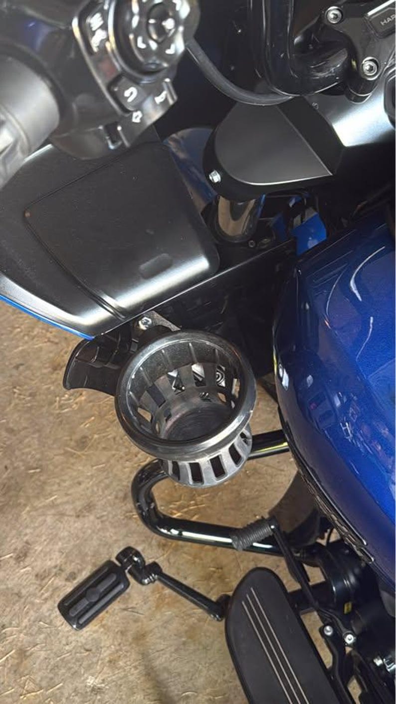Puede incluir: Primer plano de una motocicleta con un dep&oacute;sito de combustible azul y accesorios negros. Un portavasos plateado est&aacute; montado en el lateral. La motocicleta tambi&eacute;n cuenta con un reposapi&eacute;s y un manillar negros.