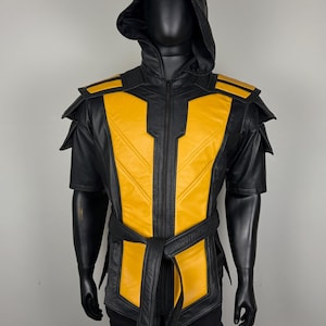 May include: Black and yellow hooded vest with a matching belt. The vest features a zip-up front and shoulder accents. The yellow panels are outlined in black. The mannequin is wearing black pants.
