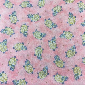 Peut inclure: Tissu rose avec un motif répété de moutons blancs avec des visages bleus et de la laine bouclée jaune. Les moutons sont dispersés sur le tissu.