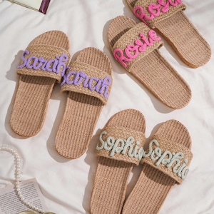 K&ouml;nnte beinhalten: Sechs Paar gewebte Sandalen mit gestickten Namen in Lila, Rosa und Hellgr&uuml;n. Die Namen "Sarah", "Rosie" und "Sophia" sind auf der Oberseite zu sehen. Die beigefarbenen Sandalen liegen auf einer wei&szlig;en Oberfl&auml;che.