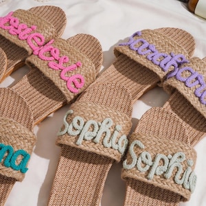 K&ouml;nnte beinhalten: Gewebte Raffia-Sandalen mit in verschiedenen Farben gestickten Namen. Die Namen sind "Emma", "Sophie", "Sarah" und "Rosie". Die Sandalen haben eine nat&uuml;rliche, neutrale Farbe. Personalisierung.
