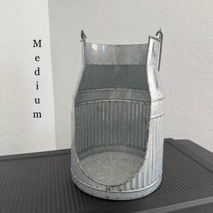 May include: A galvanized metal container with a handle, featuring a milk can design. The container has a rounded base and vertical corrugated sides. The word "Medium" is printed on the side.