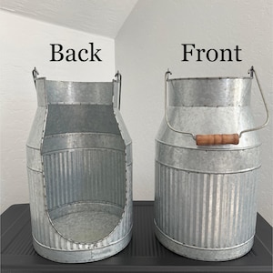 May include: Two galvanized metal milk cans with a ribbed texture. The left can is labeled Back and features a large circular cutout on the front side. The right can is labeled Front and includes a metal handle with a brown wooden grip.
