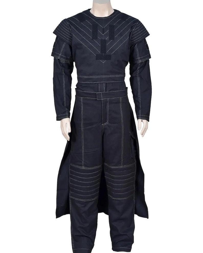 May include: A dark navy blue long-sleeved jumpsuit featuring white contrast stitching throughout. The garment includes a structured bodice with shoulder panels, a belted waist, and pleated knee sections. A long, open-sided skirt overlay extends from the waist down to the hem, creating a layered appearance.