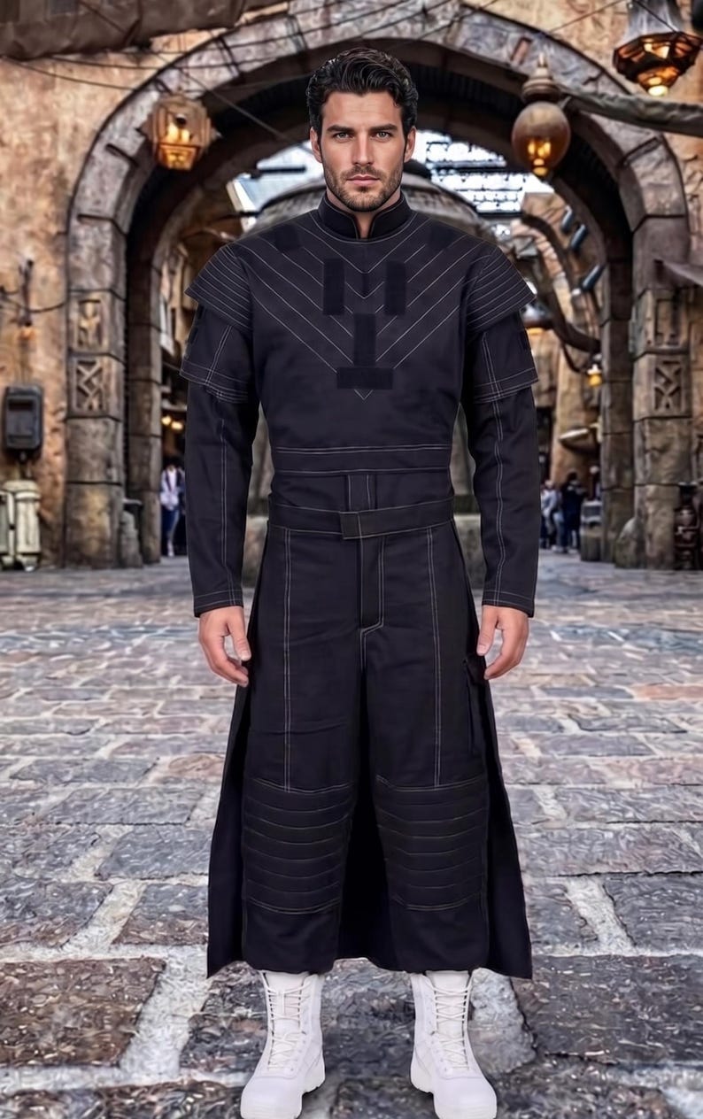 May include: A black long-sleeved tunic and matching trousers set featuring white contrast stitching, a high collar, structured shoulder panels, and a belted waist. The trousers have a layered design with horizontal quilted detailing on the lower legs.