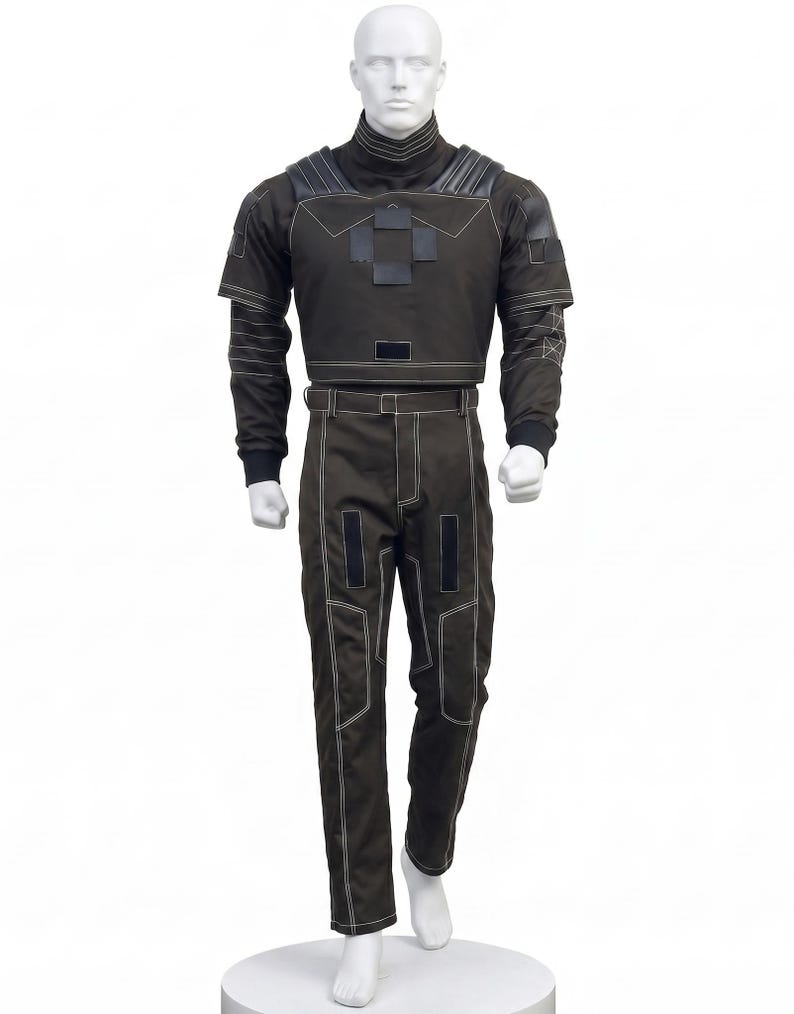 May include: A dark brown long-sleeved top and matching trousers set featuring a high collar, structured shoulder panels, and white contrast stitching. The top includes a central rectangular patch design, while the trousers feature a belt and vertical paneling details throughout the garment.