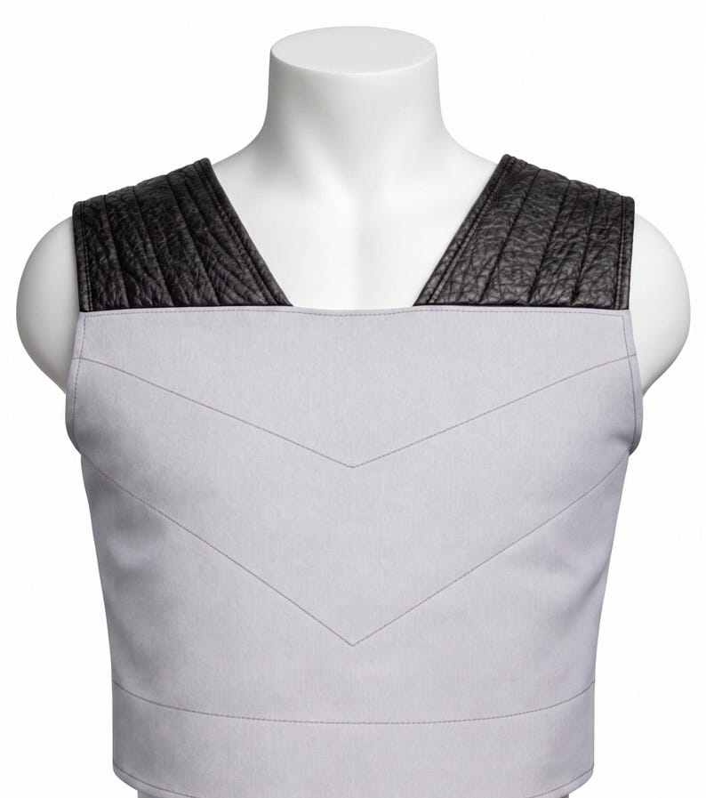 May include: A sleeveless vest featuring a light gray fabric body with a V-shaped stitched chevron pattern across the chest. The shoulders are accented with wide, black textured panels that have vertical stitching details along the top.