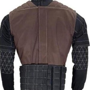 May include: A brown and black protective vest with a padded design. The vest has a brown upper section and a black lower section with adjustable straps. The sleeves are black with white geometric patterns. The vest is designed for protection.