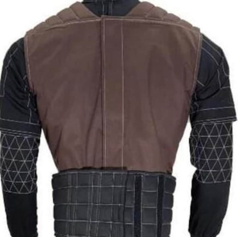 May include: A brown and black protective vest with a padded design. The vest has a brown upper section and a black lower section with adjustable straps. The sleeves are black with white geometric patterns. The vest is designed for protection.